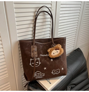 Detail van de donkerbruine shopper met borduursel van een kat en een pluche hanger