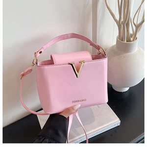 Detail of pink faux leather handbag featuring a gold V-shaped logo and adjustable strap