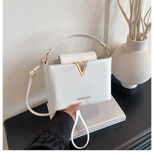 Detail of white structured handbag with gold V-shaped metal buckle and fashion logo