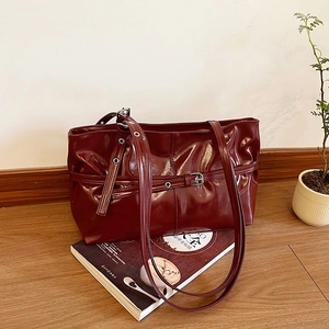 Sac cabas en cuir verni rouge foncé avec boucle argentée sur parquet vintage en bois