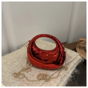 Close-up of metallic red semi-circular handbag with a gold chain on a beige sweater