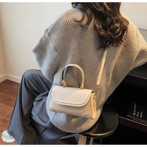 Detail view of a cream leather crossbody bag worn over a grey knit sweater