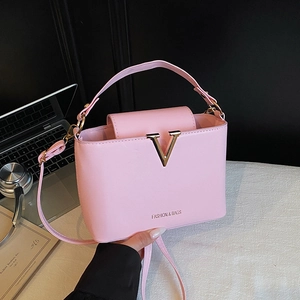 Pink leather bucket bag with gold V buckle and shoulder strap on a white desk