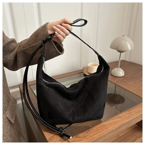 Detail of black suede hobo bag with silver zipper and slim leather strap on wooden table