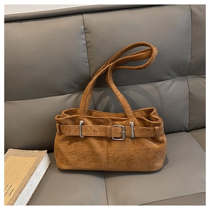 Detail of vintage brown suede shoulder bag with metal buckle on a gray sofa
