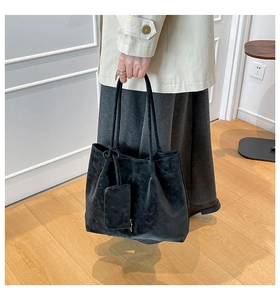 Detail of a large black suede tote bag with matching pouch and dual handles in use