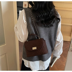Detail of a dark brown quilted crossbody bag with a gold metal twist lock and chain strap