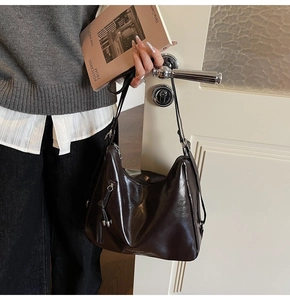 Detail of dark brown leather tote bag hanging on door with fringe and zipper accents