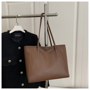 Detail of dark brown faux leather tote bag hanging on a rack with a tweed jacket