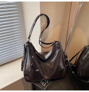Close-up of glossy brown leather tote bag featuring a vertical zipper and tassel detail