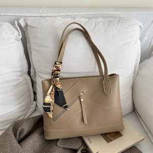 Chique beige leren tote bag met zijden sjaal aan handvat op een witte bank