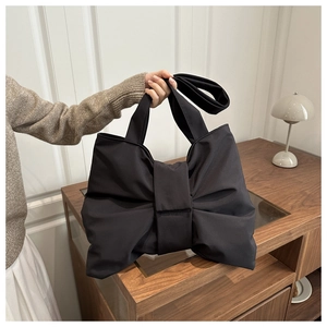 Detailed view of black oversized bow shoulder bag on a minimalist wooden cabinet