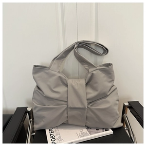 Detail of light grey bow-shaped handbag with dual straps on a black chair