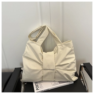 Creamy white soft leather shoulder bag with bow details on a minimalist black chair
