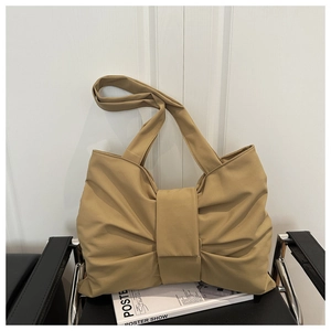 Close-up of khaki bow-shaped tote bag with pleated faux leather on a black seat