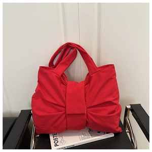 Detail of red fabric tote bag featuring a large bow-shaped pleated design on a black chair