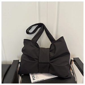 Detail of a black nylon tote bag featuring a large bow design on a leather chair