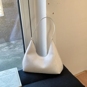 White snakeskin textured hobo bag with slim shoulder strap displayed on a black stand