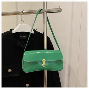 Detail of glossy green patent leather baguette bag with golden metal clasp on black jacket