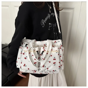 Detailed view of white corduroy shoulder bag with cherry print and multiple zip pockets