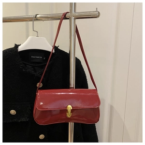 Detail of burgundy patent leather bag with gold buckle on shoulder strap and rectangle shape