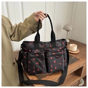 Detail of cherry print black tote with multiple zip pockets held by model in warm setting