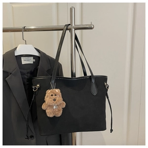 Detail of black tote bag with leather straps and a cute brown plush bear charm