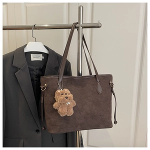 Detail of dark brown suede tote bag featuring a plush bear charm and leather straps