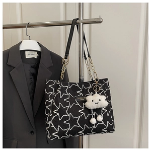 Detail of black tote bag with white star stitching, gold chain strap, and cloud charm