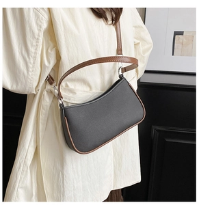 Detail van zwarte lederen baguette tas met bruine riem gedragen op een trenchcoat
