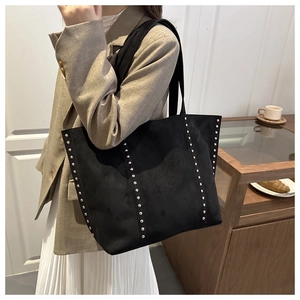 Detail of a black suede tote bag featuring silver rivet decorations and dual shoulder straps