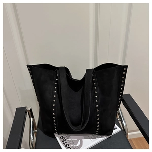 Detail of black suede tote bag with silver metal studs placed on a modern chair