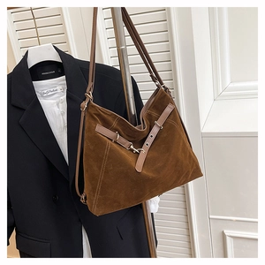 Close-up of a dark brown suede tote bag featuring adjustable belts and metal hook buckles