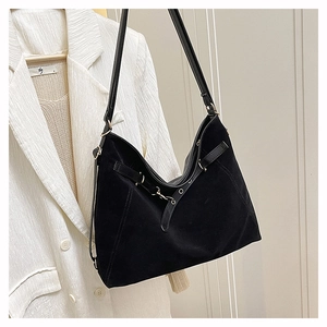 Detail of black suede tote bag with metal buckle and leather strap on white blazer