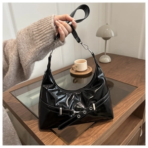 Detail of black glossy patent leather underarm bag with silver buckle and pleated texture