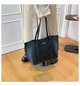 Detail of black tote bag featuring matte leather texture and gold embossed fashion lettering