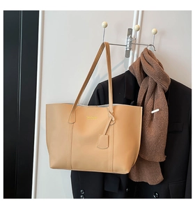 Detail of light apricot tote bag with golden logo and pendant on a coat hanger