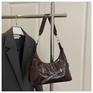 Detail of dark brown glossy patent leather underarm bag with metal buckle on a hanger