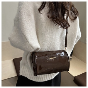 Detail of a dark brown patent leather cylinder bag with gold fashion lettering logo