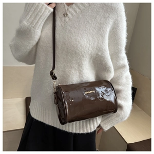 Detail of a dark brown patent leather cylinder bag with gold Fashion logo and slim strap