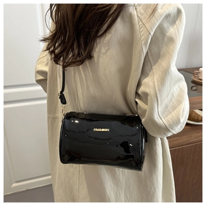 Detail of black patent leather cylinder bag with gold fashion text and slim strap