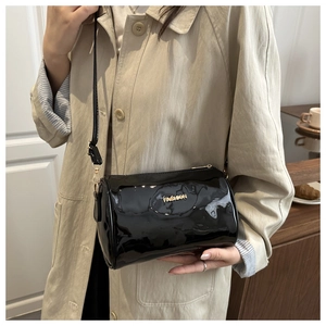 Close-up of black patent leather cylinder bag with gold fashion letter logo detail