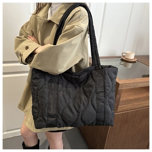 Quilted black nylon tote bag shown on model wearing a khaki trench coat and boots