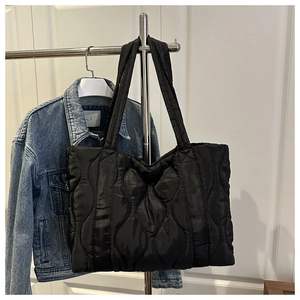 Detailed view of large black quilted tote bag with wave stitching hanging on a metal hanger