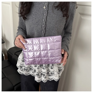 Detail of purple metallic quilted clutch bag held by model showing shiny fabric texture