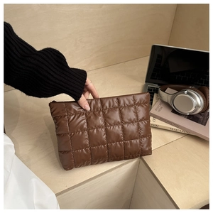 Close-up of brown quilted nylon pouch held by hand against a modern office background