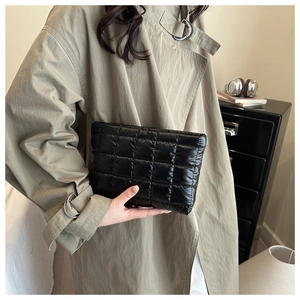 Chic black quilted clutch bag held by model wearing a trench coat in minimalist setting
