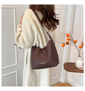 Close-up of brown lychee grain leather tote bag with gold lettering on a soft coat