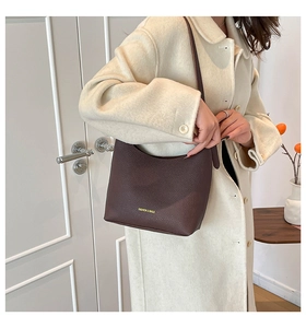 Deep brown pebble leather bag detail with gold lettering worn on a white wool coat