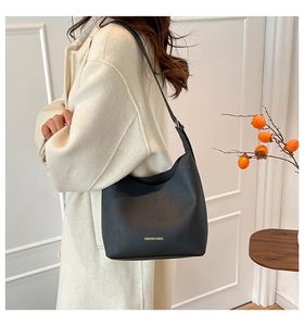 Detail of black lychee grain leather bucket bag with gold fashion text and long shoulder strap